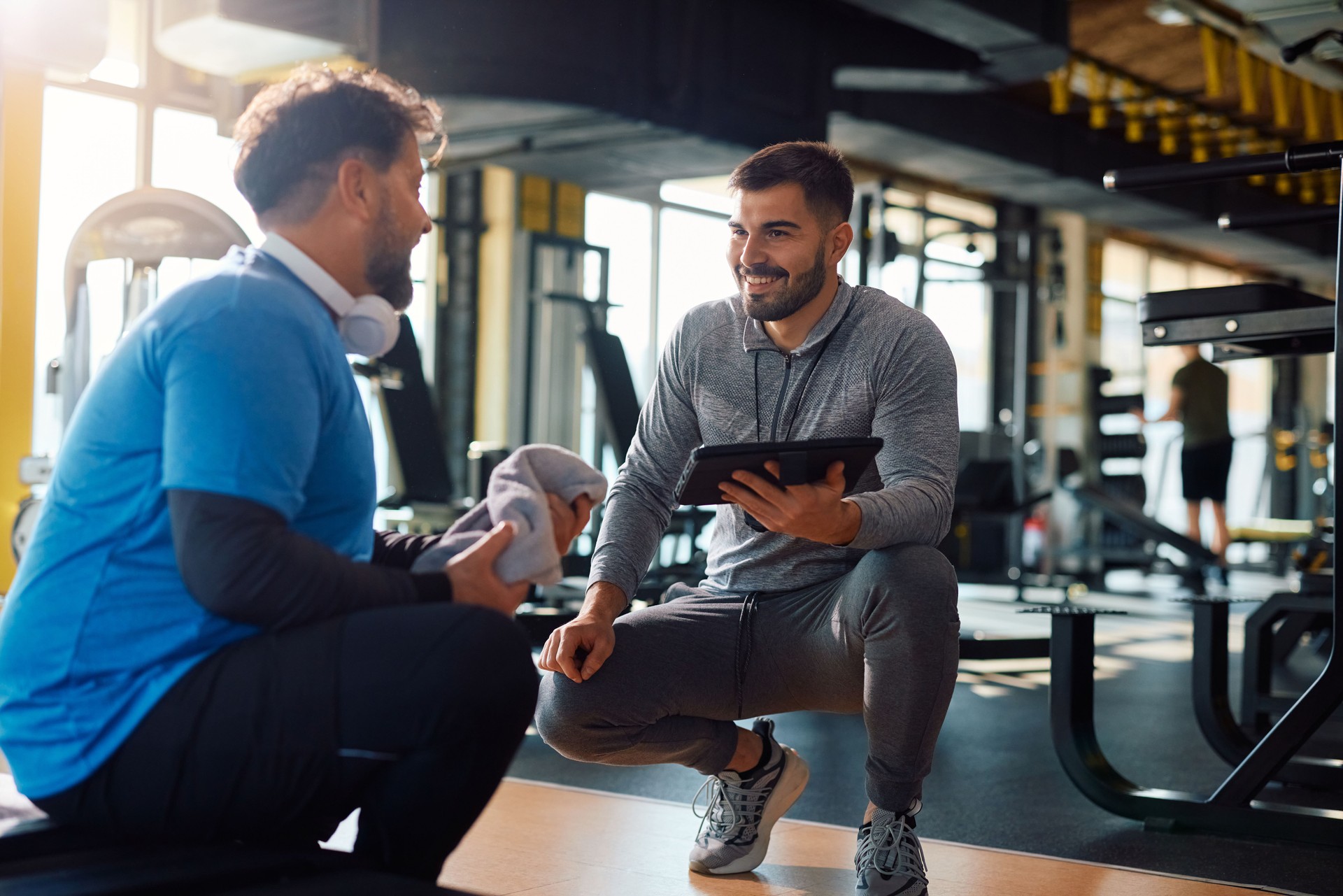 Fitness instructor using touchpad while talking to mature man during exercise class in a gym.